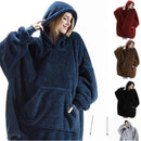 Person wearing an oversized fleece blanket hoodie, sitting on a couch in a cozy indoor setting with soft lighting.