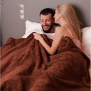 Cozy couple snuggled under a thick waterproof winter blanket on a bed, showcasing soft texture and king-size coverage.